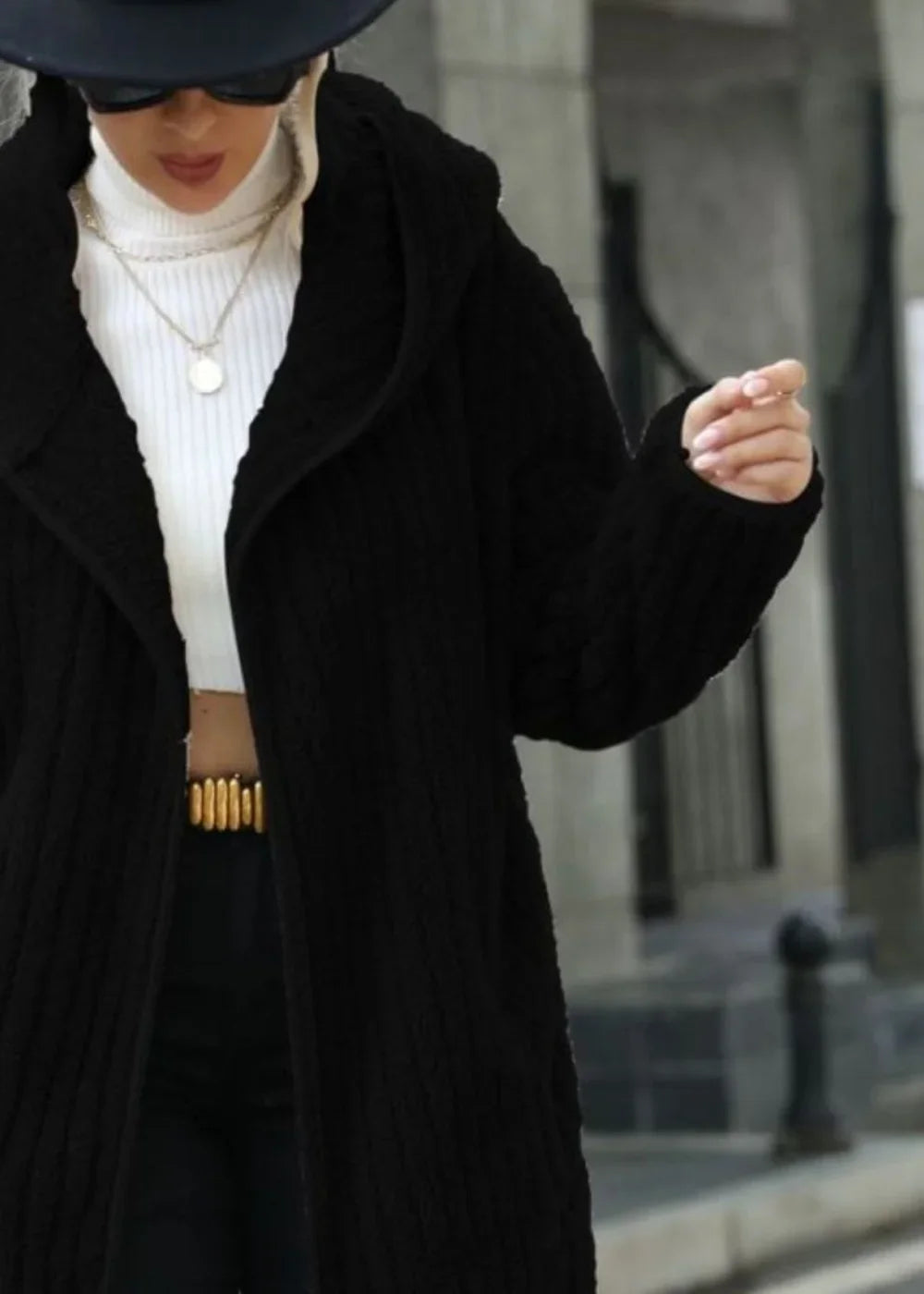 Black textured knit hooded long cardigan on model, worn over a white turtleneck and gold belt.