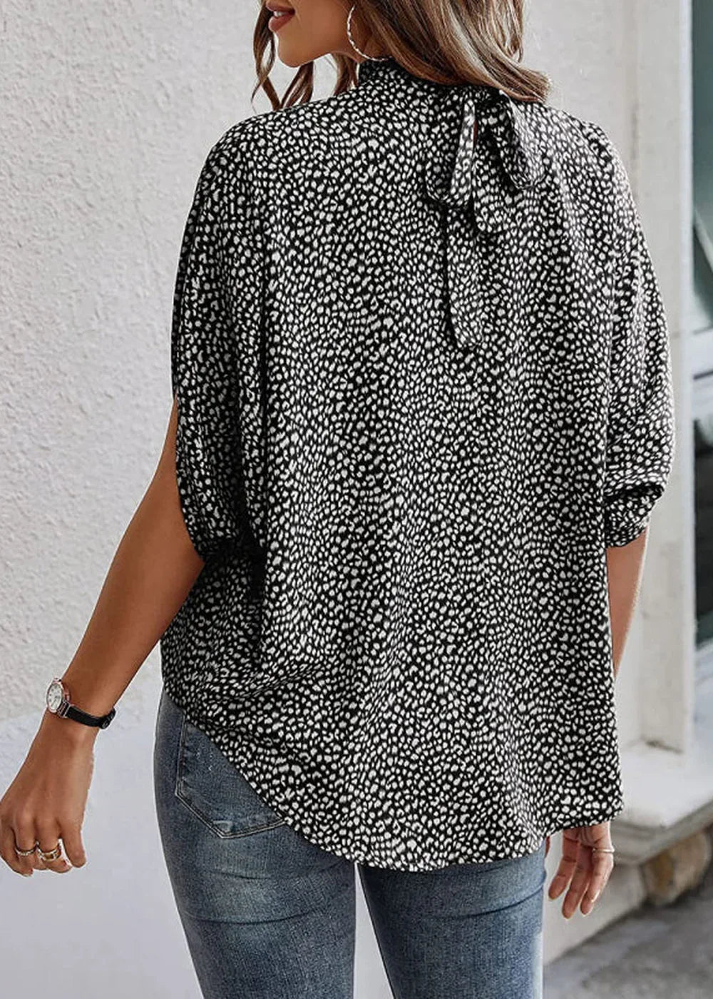 Back view of a black and white polka dot print blouse with a tie detail at the neck on a model.