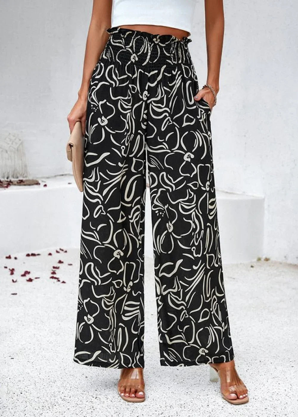 Black wide-leg pants with a white abstract floral print and smocked waistband, worn by a model.