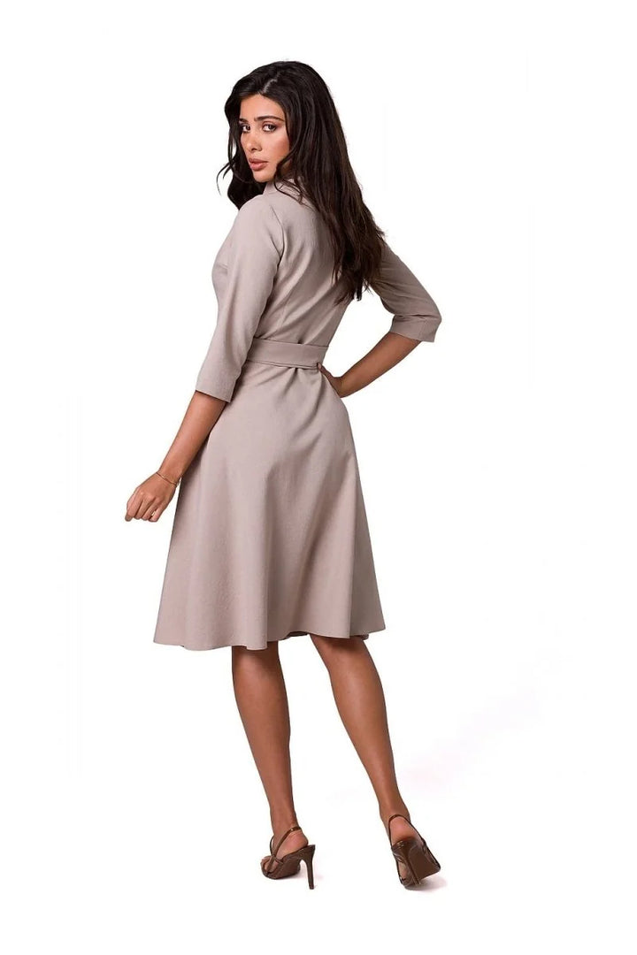 Woman in a taupe midi dress with a belted waist and 3/4 sleeves, wearing brown heeled sandals.