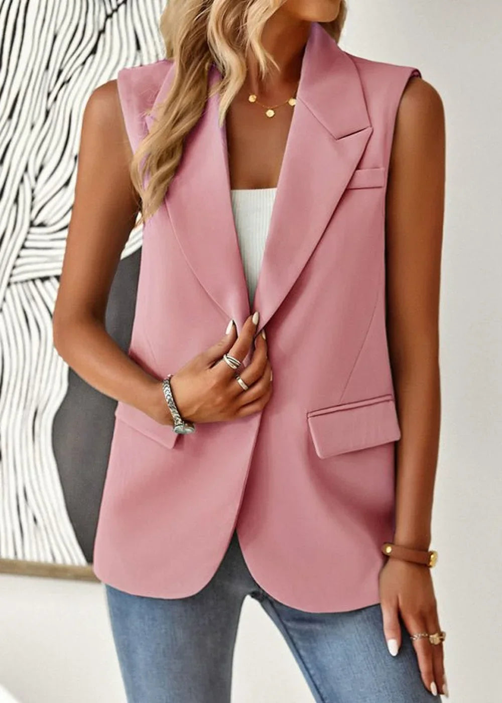 Pink sleeveless blazer with a notched lapel, worn by a model with jeans and jewelry.