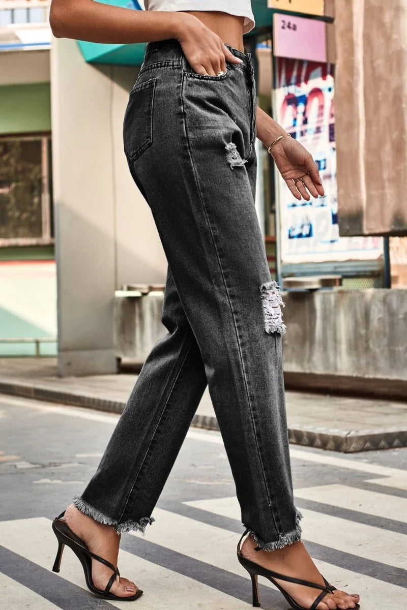 Woman walking in loose-fit, charcoal grey distressed denim jeans with frayed hems and a cropped white top.