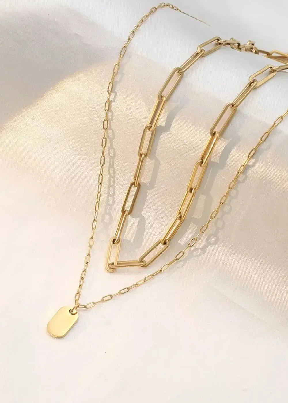 Gold-plated layered necklaces with rectangular links and a small oval tag.