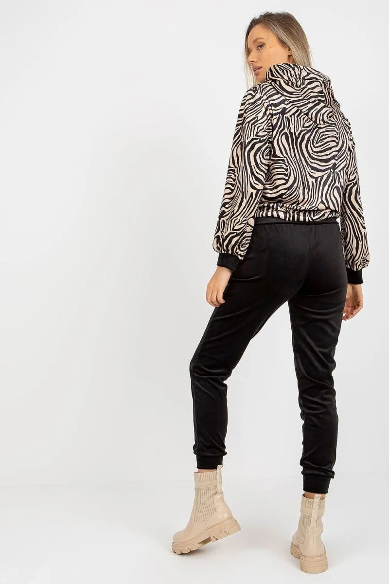 Woman from behind in black velvet pants with a zebra print jacket and beige boots.