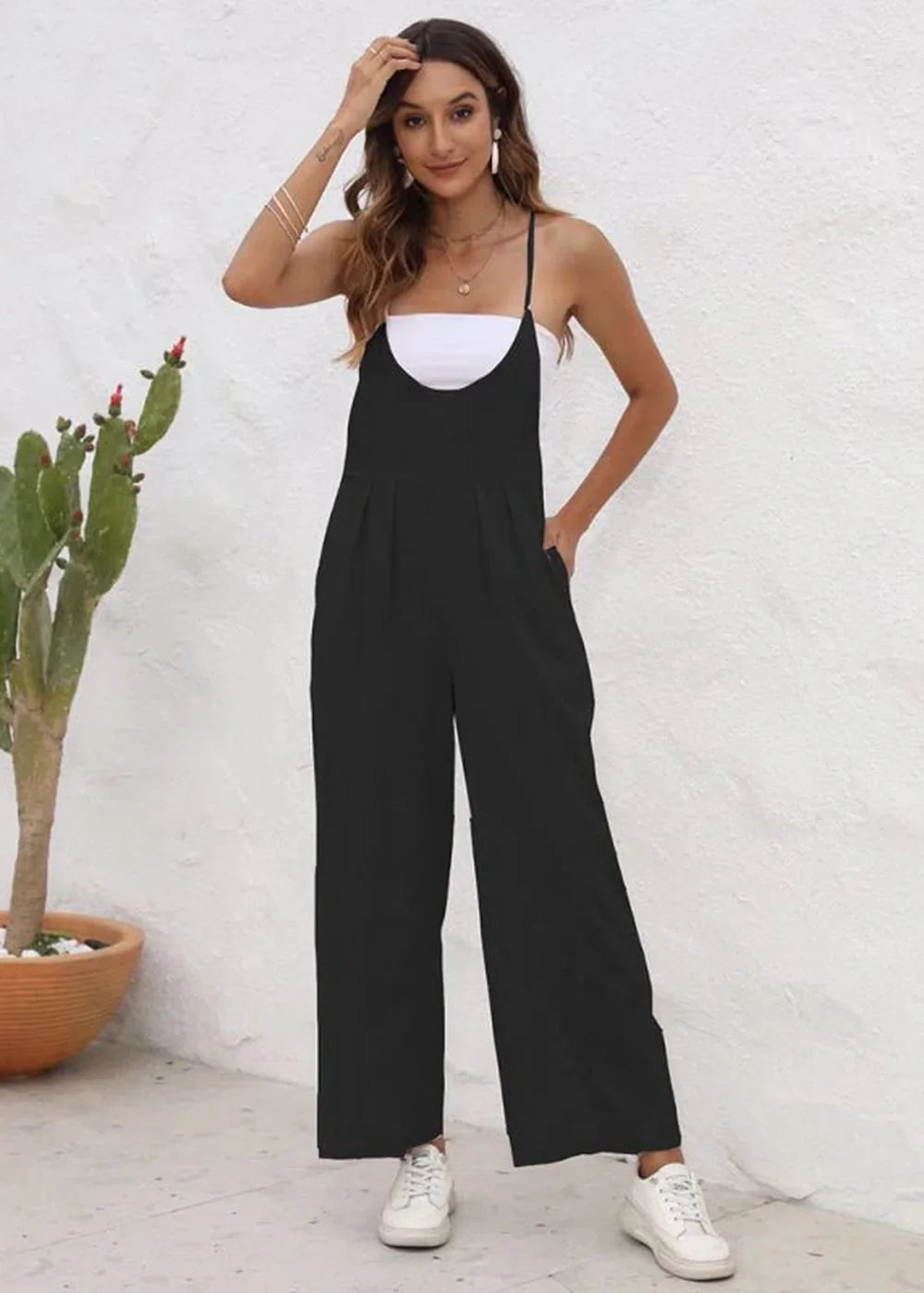 Black wide-leg jumpsuit with spaghetti straps, white top, and white sneakers on a model.