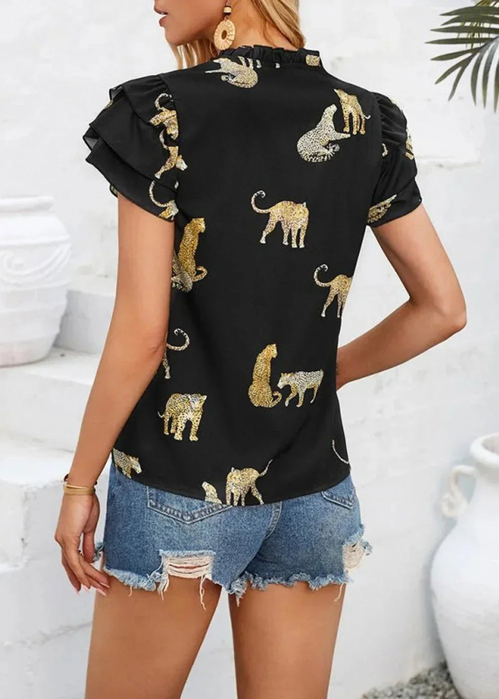 Black top with all-over gold leopard print, ruffled short sleeves, and a high neckline, worn with distressed denim shorts.
