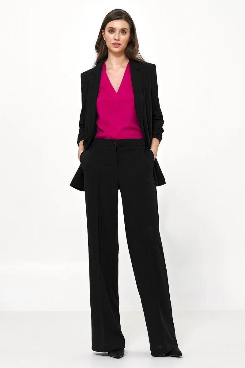 Full-length view of a woman wearing black wide-leg pants and a black blazer over a bright pink V-neck top.