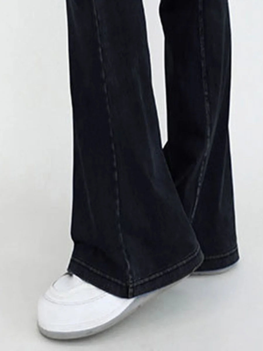 Close-up of dark wash flared jeans with white sneakers, showing hem and stitching detail.