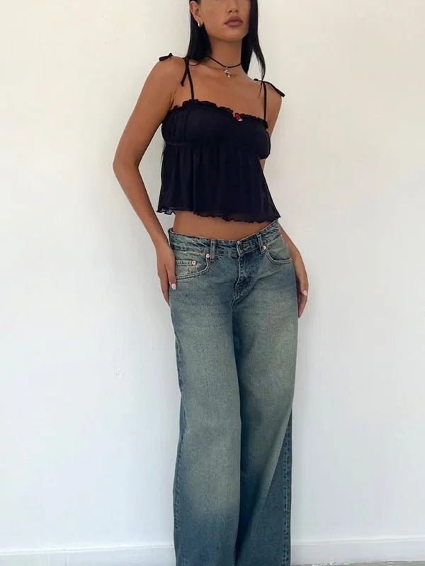 Black ruffled cami with floral detail and low-rise distressed jeans on a model.