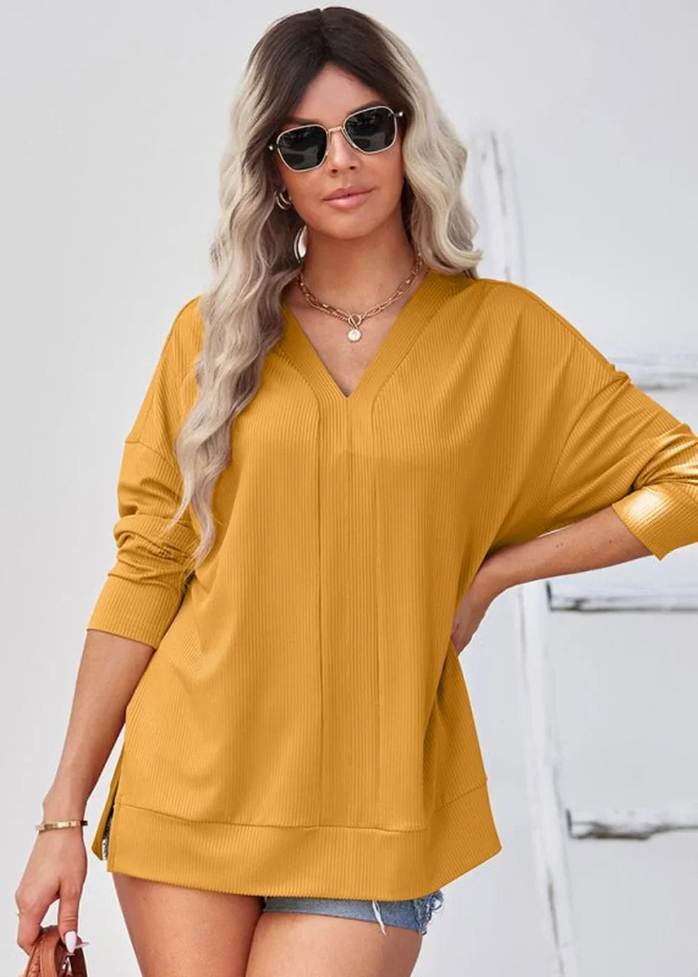 Mustard yellow ribbed V-neck top with dolman sleeves and side slits on model.