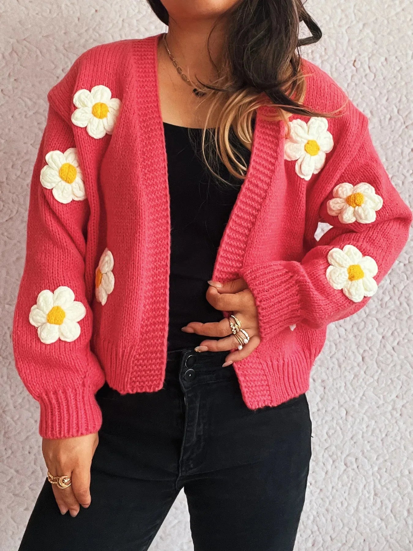 Pink knitted cardigan with white and yellow floral appliques, worn by a model.