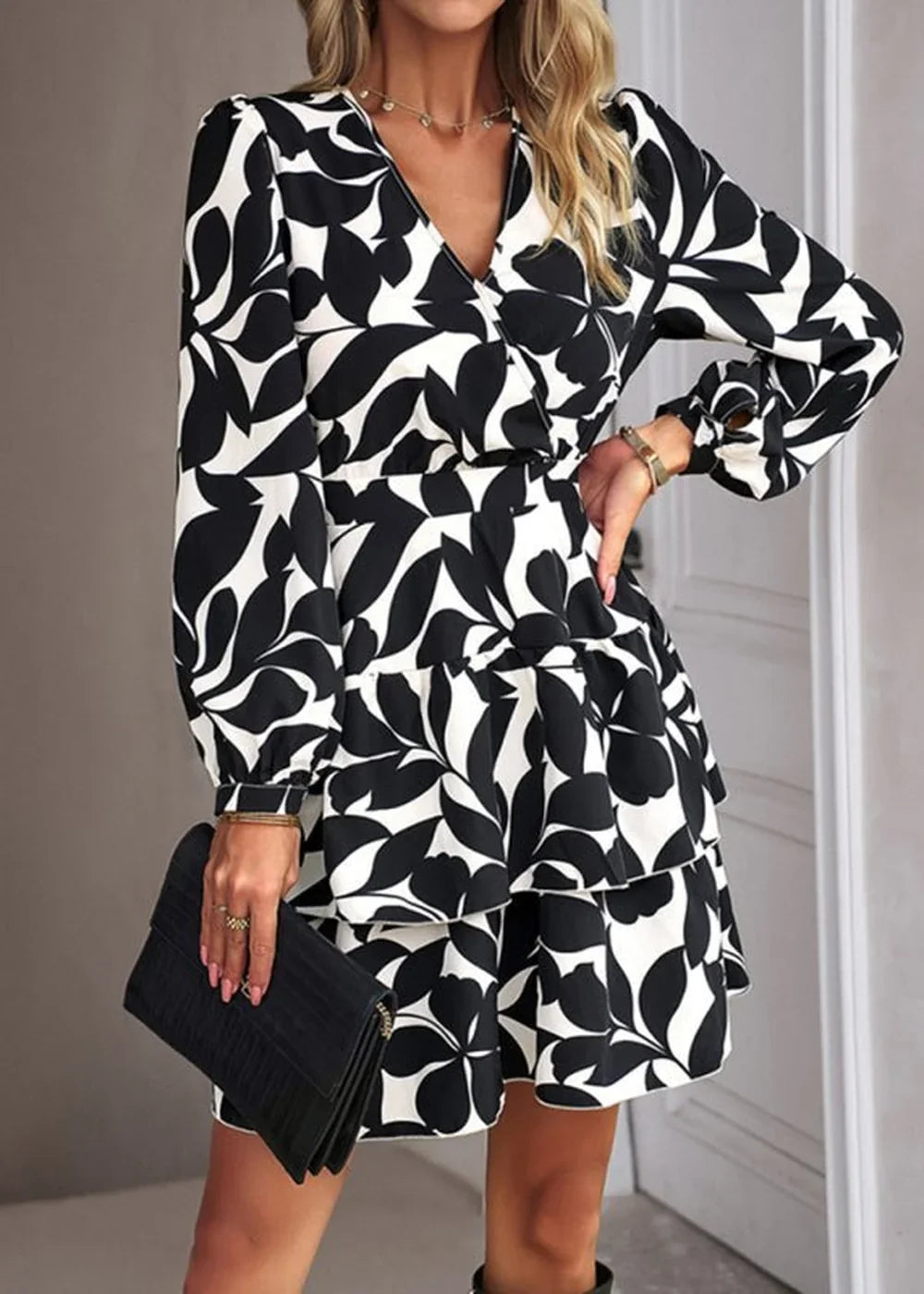 Black and white leaf print dress with tiered ruffles and long sleeves, held by a model with a clutch.