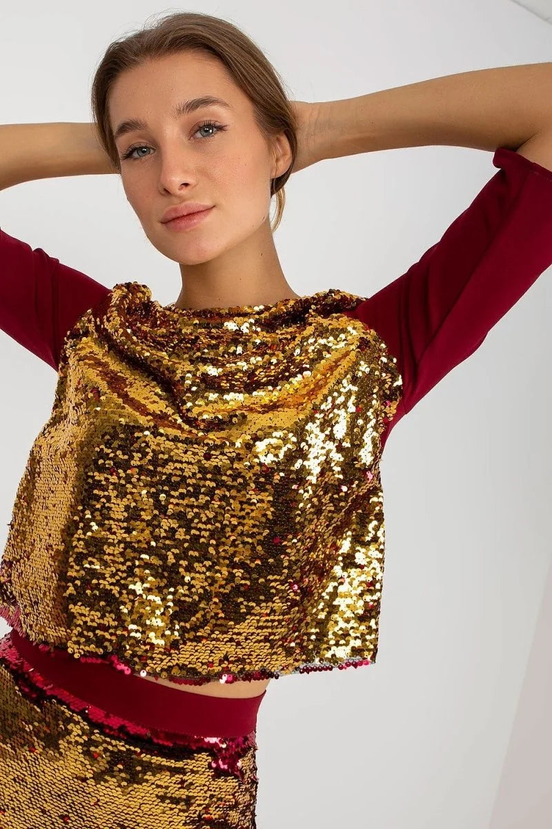 Gold sequin top with burgundy sleeves and a cowl neck, worn by a model with hands behind her head.