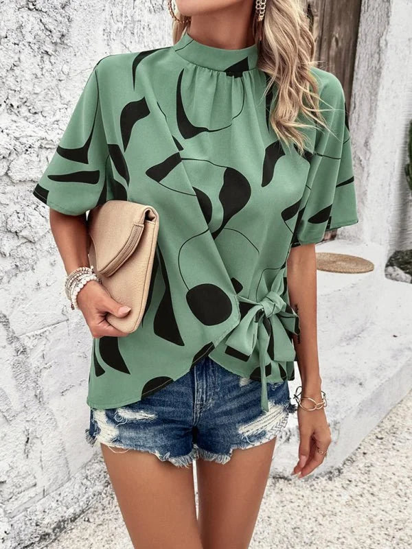 Green abstract print tie-waist blouse with short sleeves, paired with distressed denim shorts.