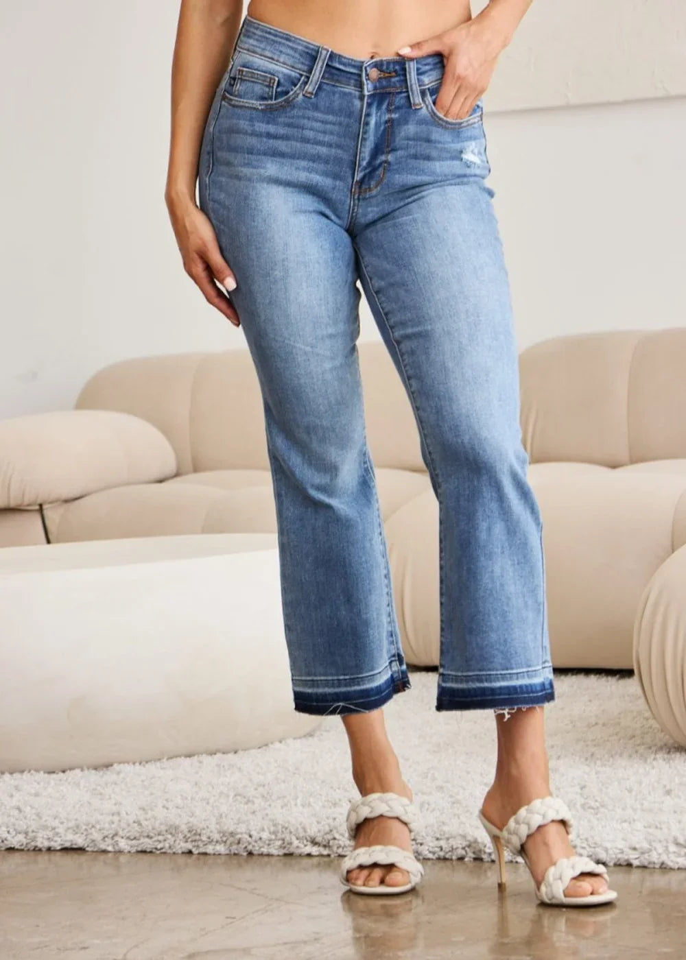Medium wash denim jeans with a frayed hem and a distressed detail on the right thigh.