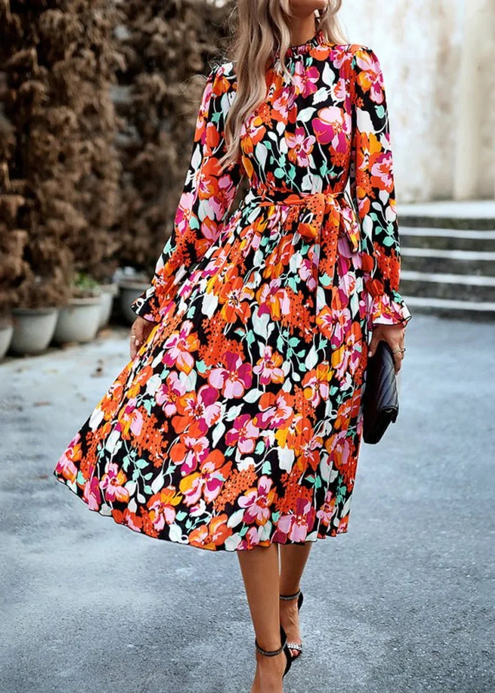 Woman in a vibrant, multi-colored floral print midi dress with long sleeves and a cinched waist.