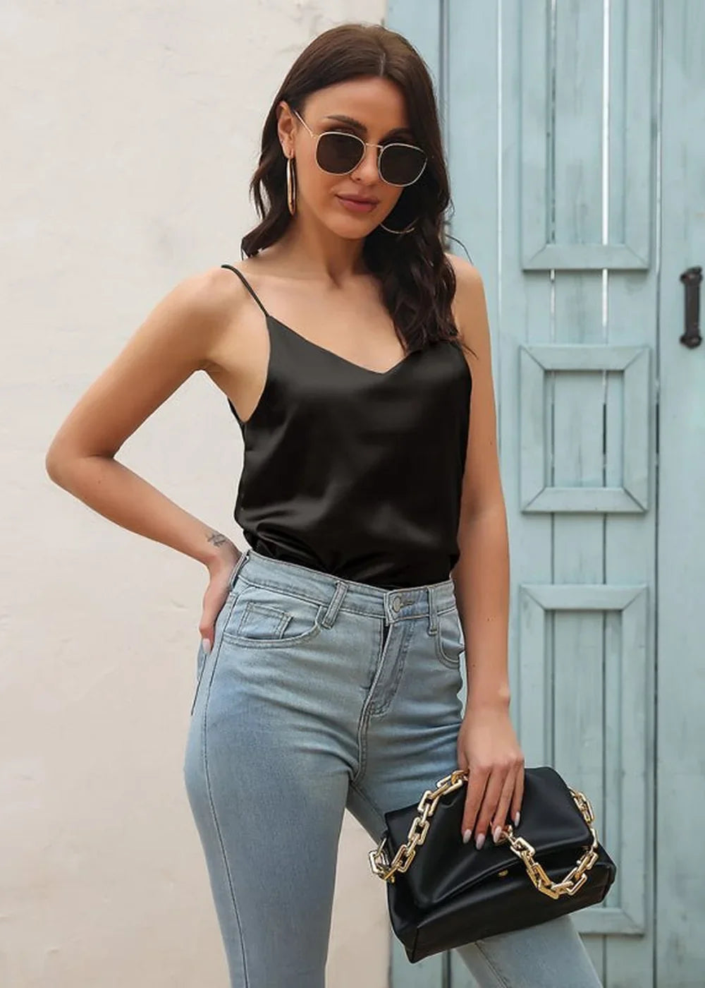 Black satin cami top with spaghetti straps, paired with light wash denim jeans and a black clutch with a gold chain.