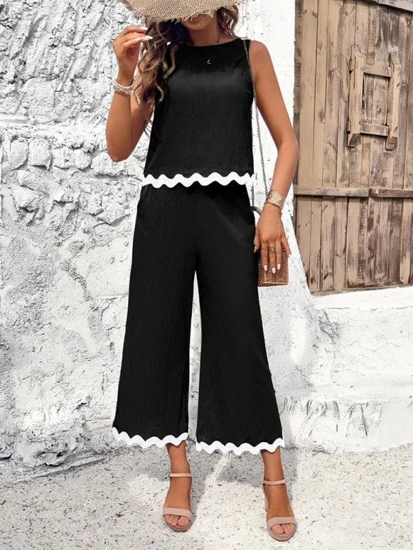 Black sleeveless wide-leg jumpsuit with scalloped white trim and wide straps.