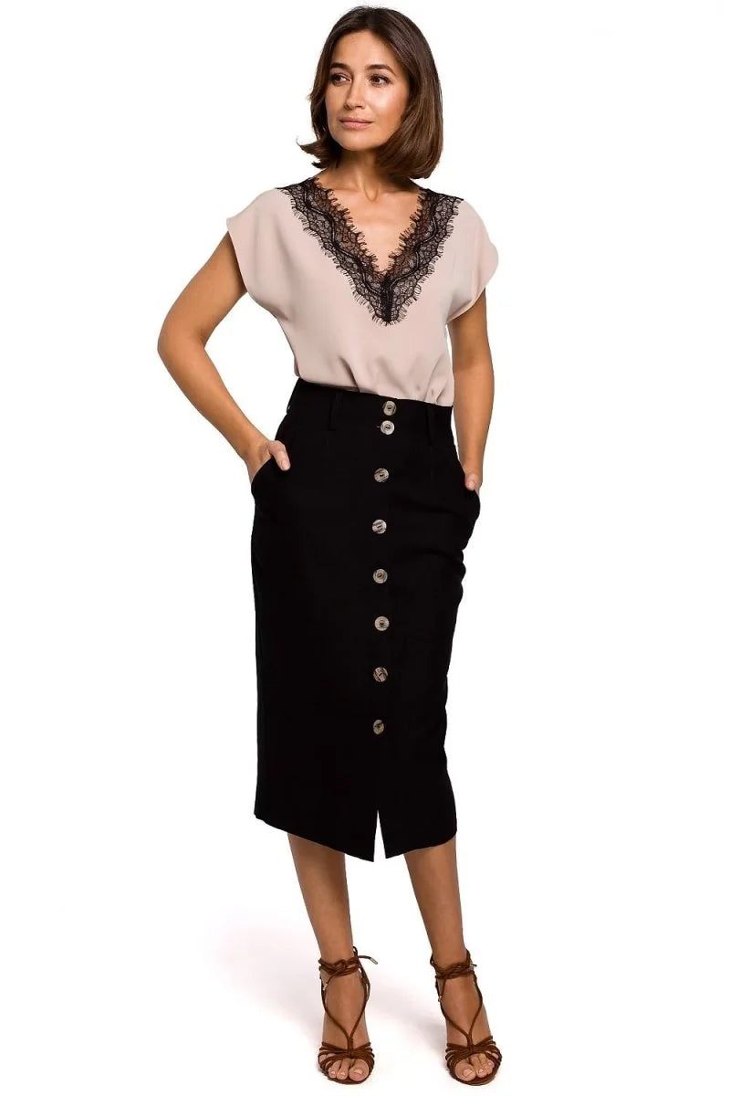 Full-length shot of a woman wearing a beige V-neck top with black lace trim and a black button-front midi skirt.
