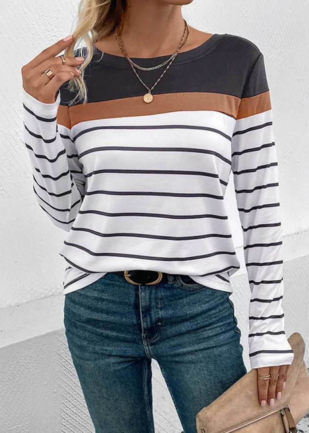 Long-sleeve striped top with brown, black, and white bands, paired with blue jeans and gold necklaces.