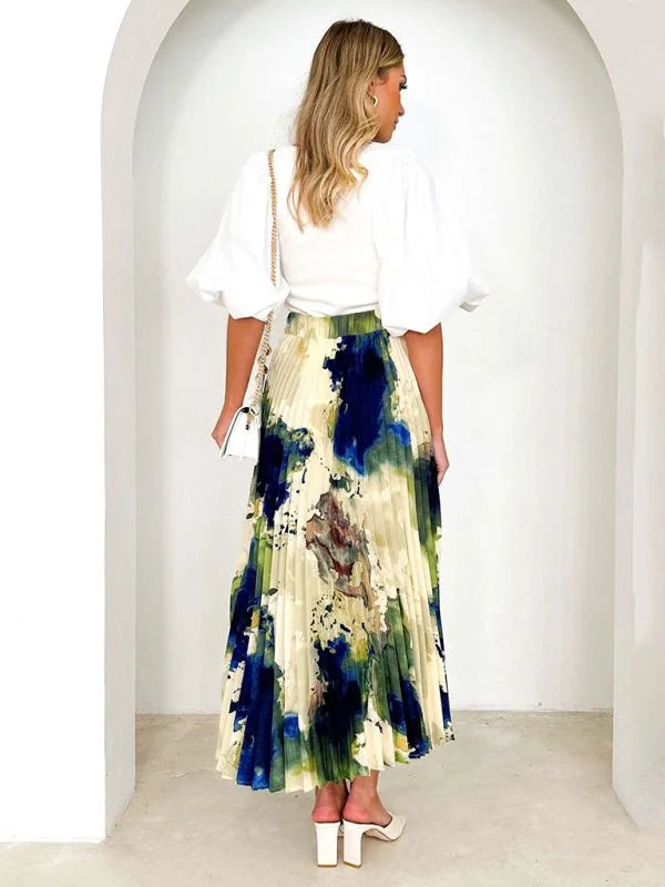 Flowy midi skirt with a watercolor print in shades of blue, green, and beige, featuring pleats and a high waist.