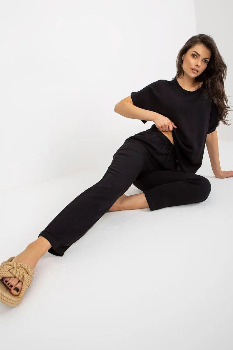 Model in black cotton blend pants with drawstring waist and braided tan slides.