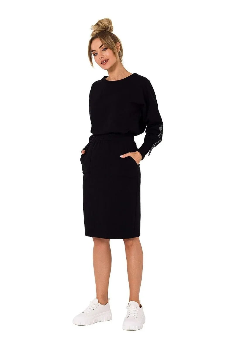 Full-length black cotton-blend midi dress with crew neck and long sleeves, worn by a model with white sneakers.