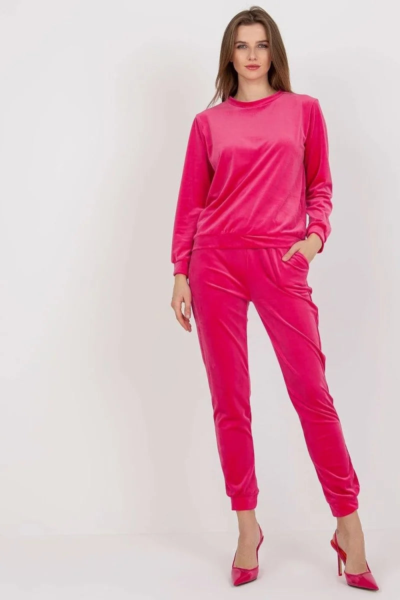 A woman models a bright pink velvet tracksuit with a crew neck sweatshirt and jogger pants.