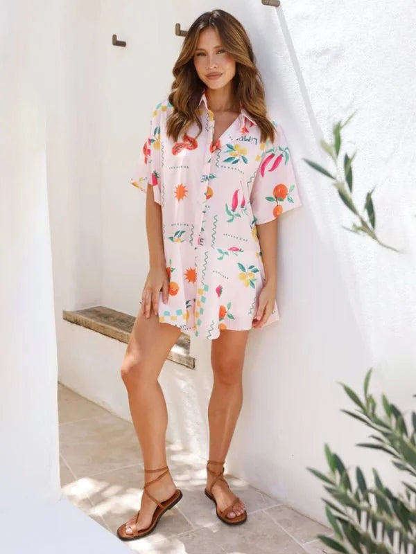Light pink short-sleeve shirt dress with a playful fruit and chili pepper print, worn by a model with strappy brown sandals.