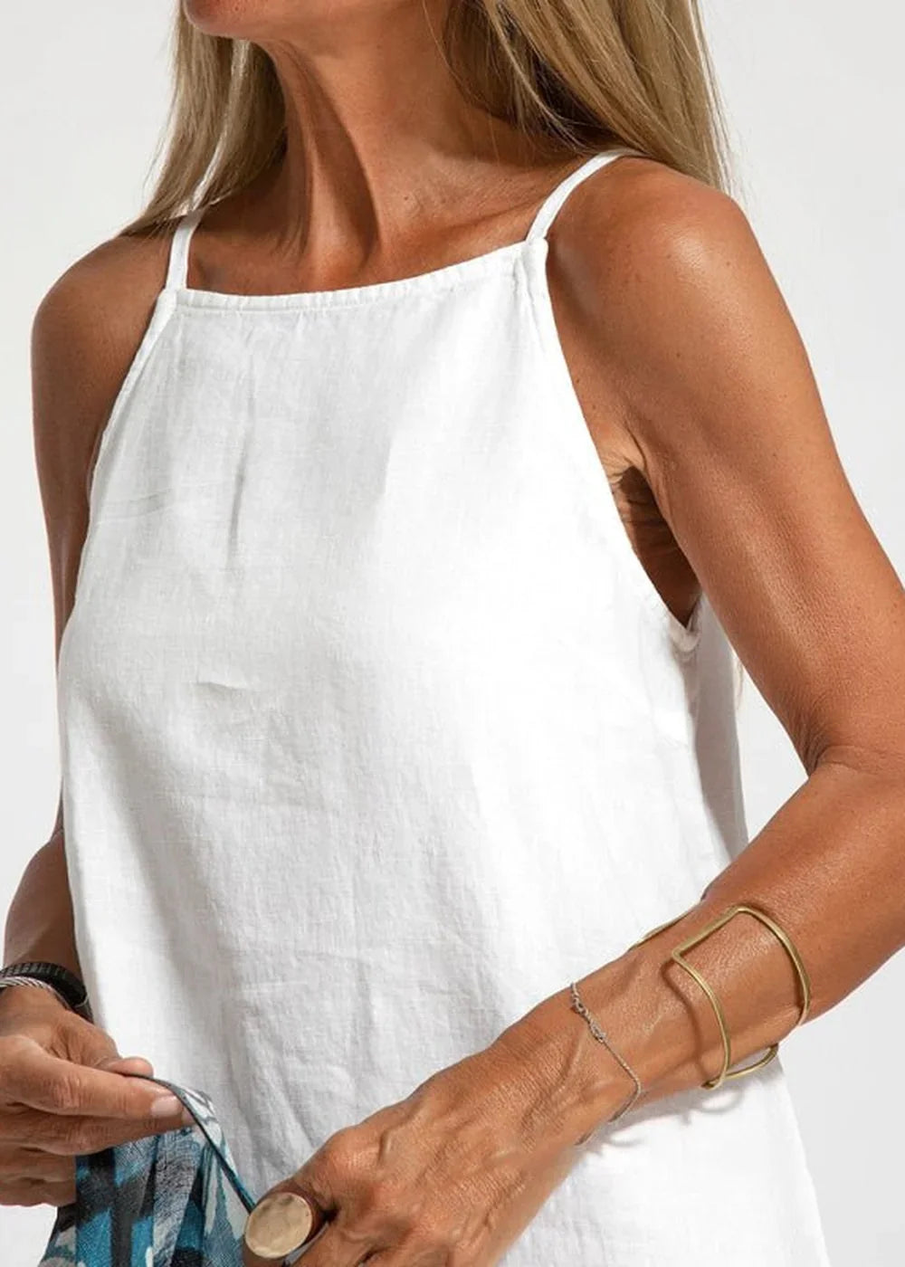 Woman in a white linen-blend tank dress, showing arms with gold cuff and silver bracelet.