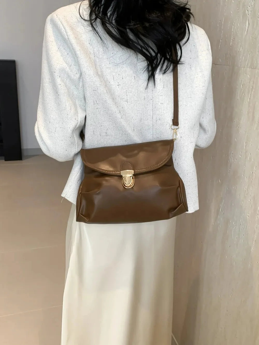 Brown leather crossbody bag with gold clasp, worn over a white textured blazer.