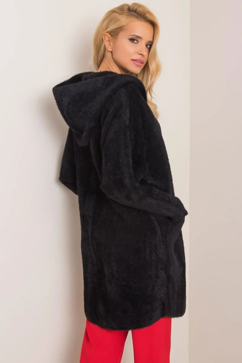 Black fuzzy hooded cardigan with pockets, worn by a model with red pants.