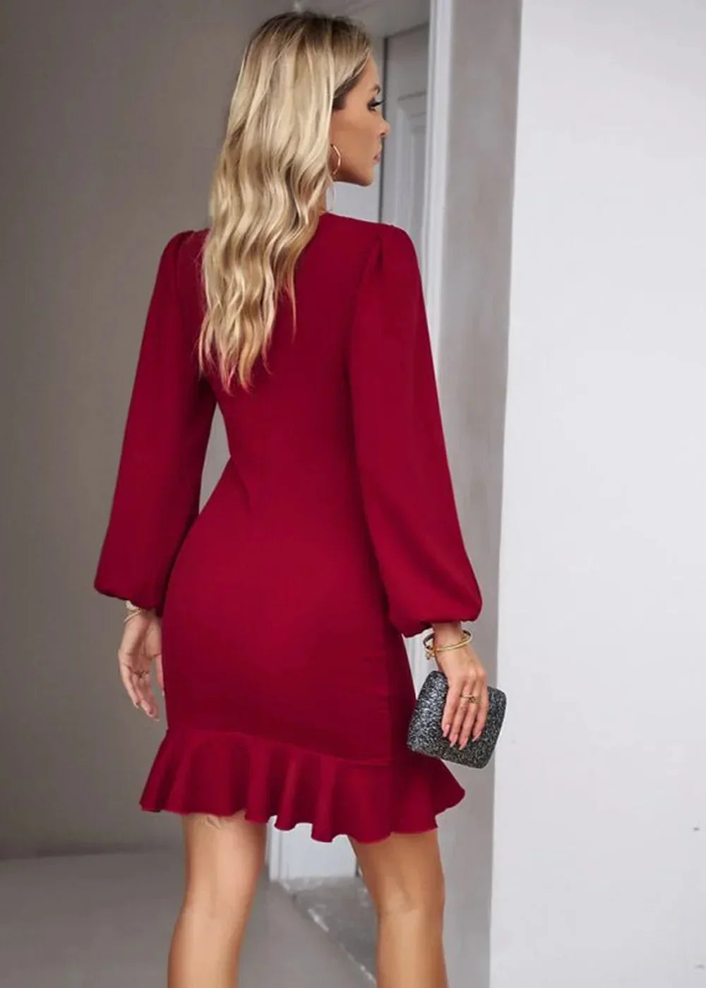 Woman in a red, long-sleeved dress with a ruffled hem, holding a small black clutch.