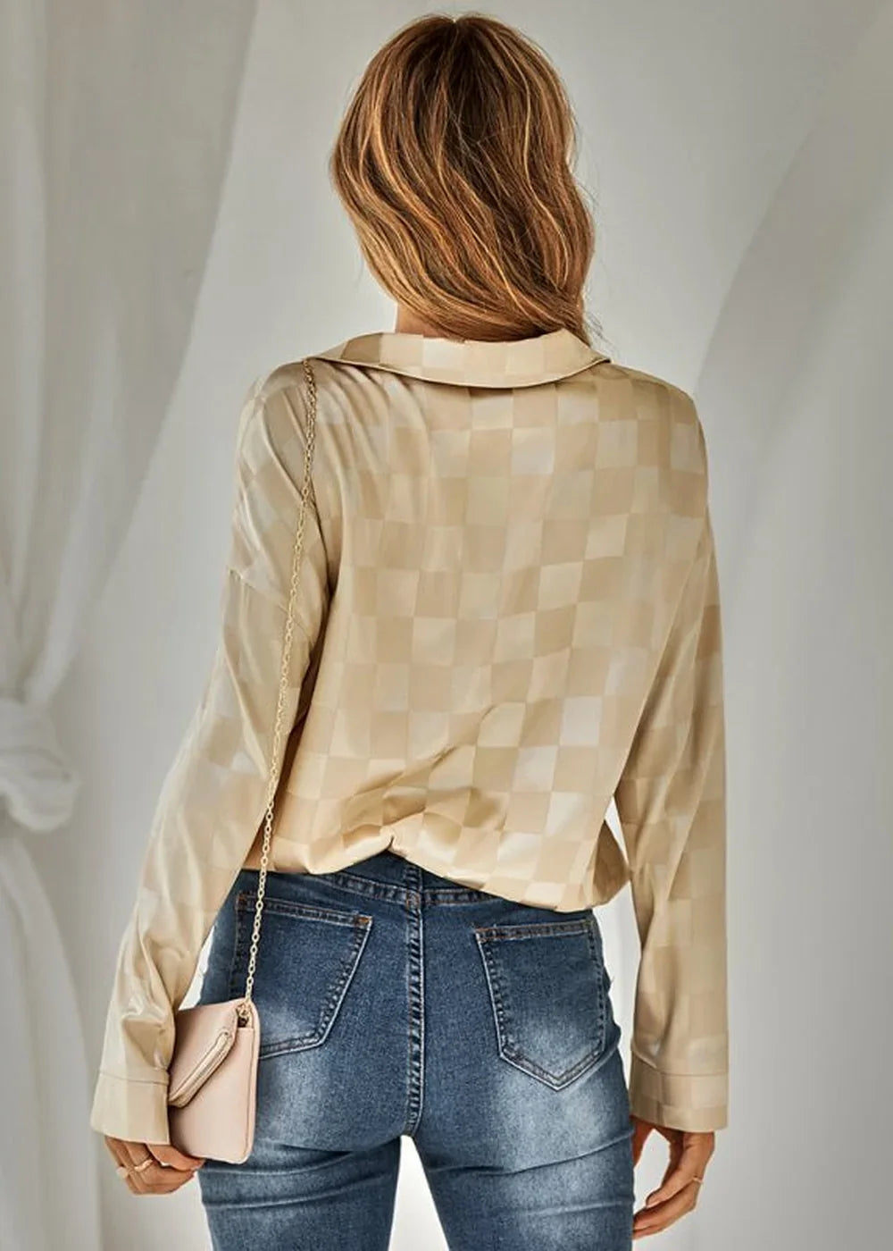 Woman from behind wearing a beige checkered long-sleeved top and blue jeans, carrying a small pink purse.