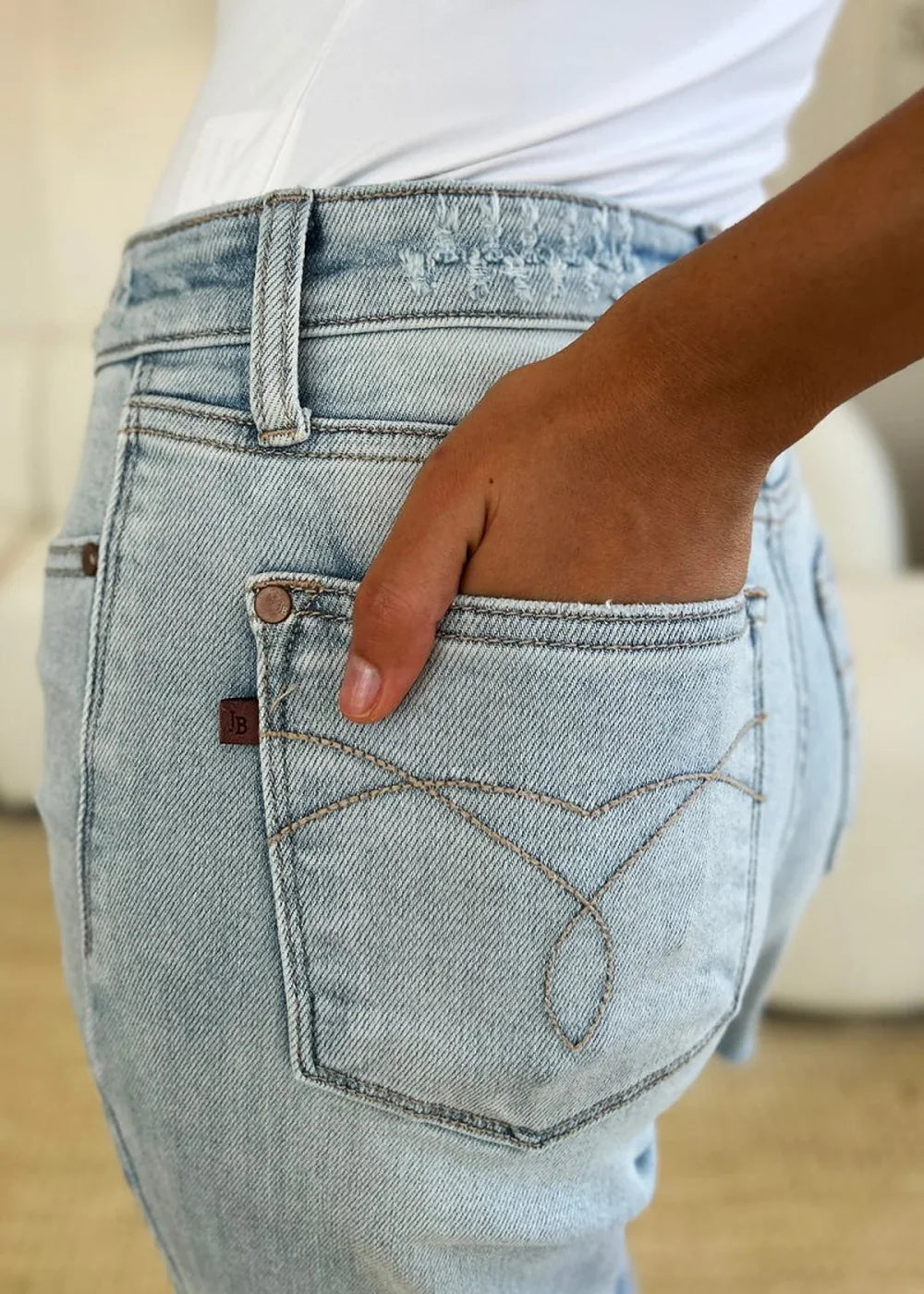 Close-up of light-wash distressed denim jeans with a brown leather patch and decorative stitching on the back pocket.