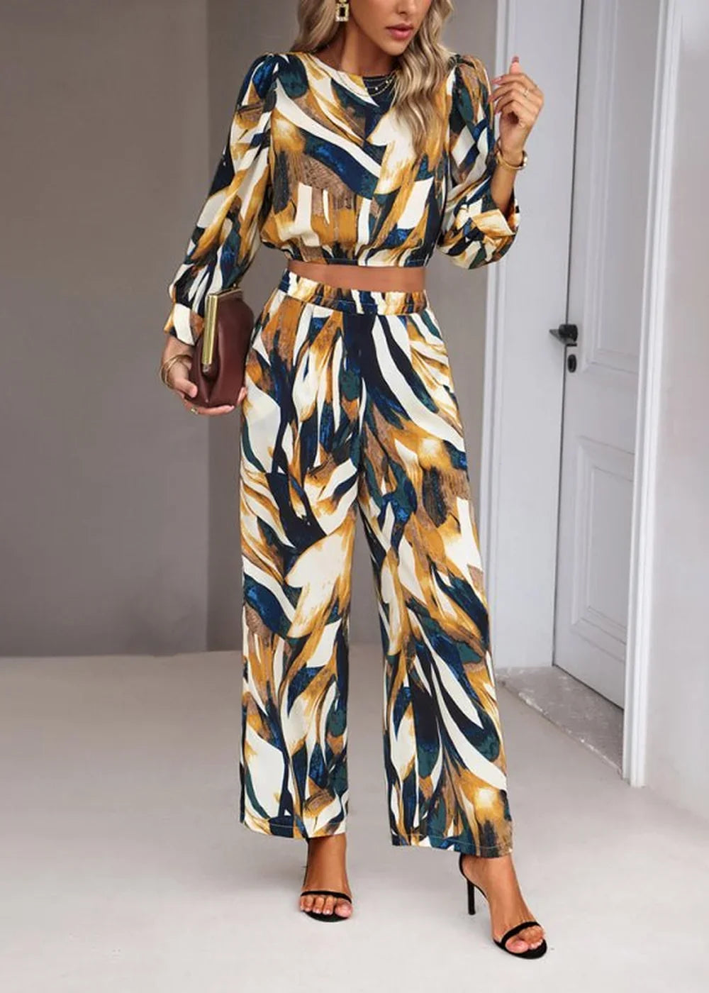 Woman in a long-sleeved crop top and wide-leg pants with a brown, blue, and white abstract print.