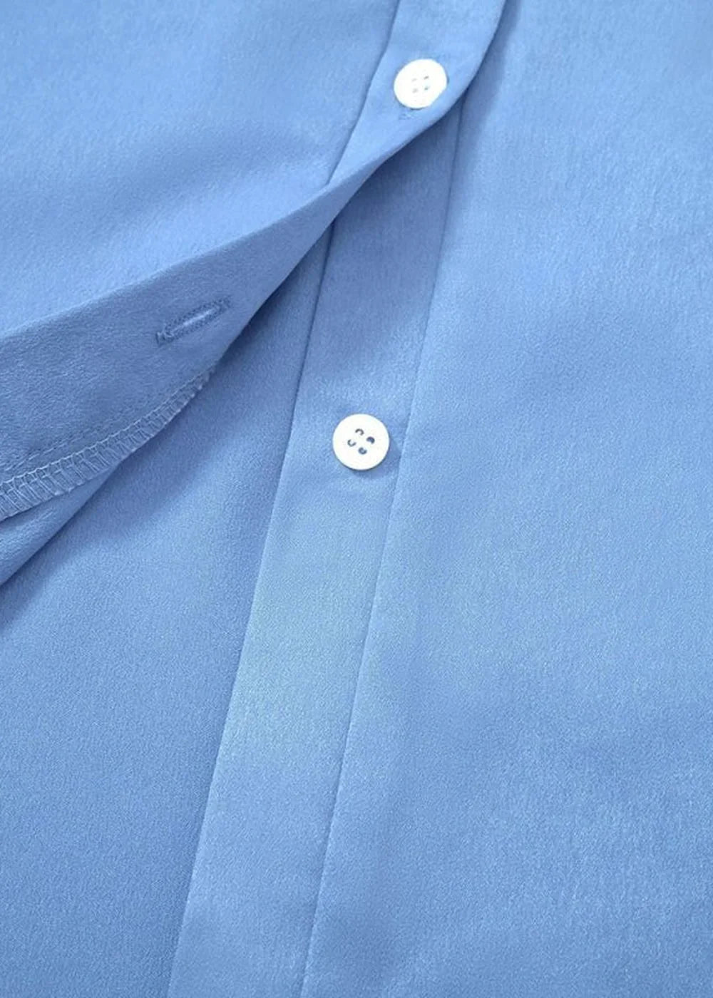 Close-up of a light blue polyester shirt with white buttons and a fabric texture.