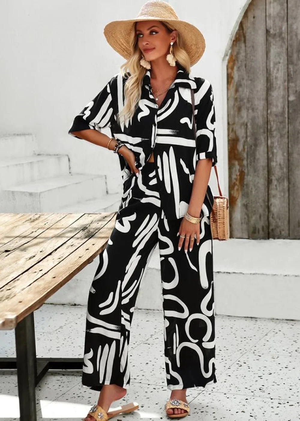 Black and white abstract print wide-leg pant suit with straw hat and woven bag.
