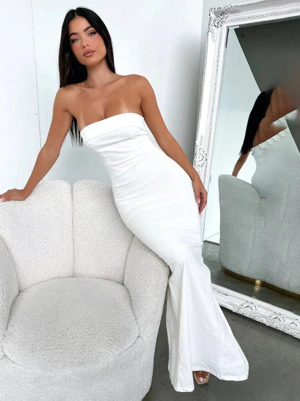 White strapless mermaid gown with a ruched bodice, a floor-length hem, and a textured fabric, worn by a model sitting in a...