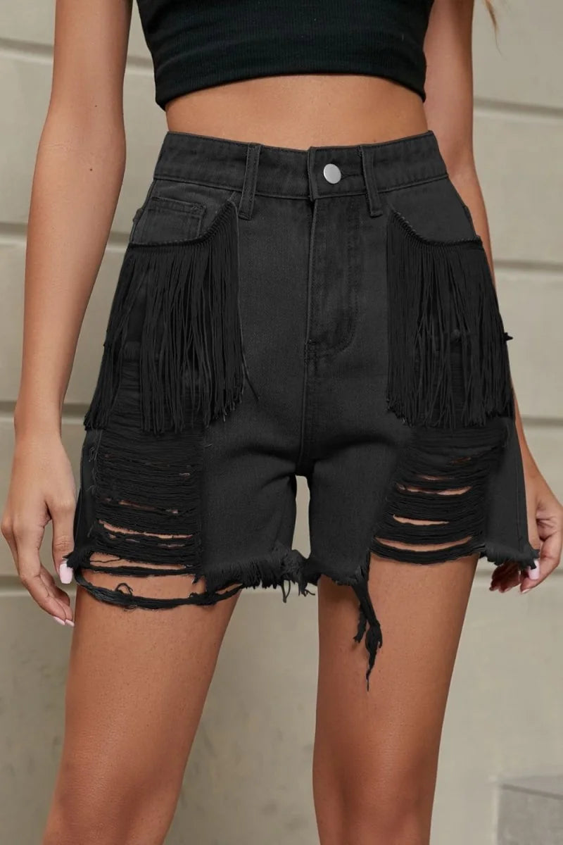Black distressed denim shorts with fringe trim and ripped details on a model.