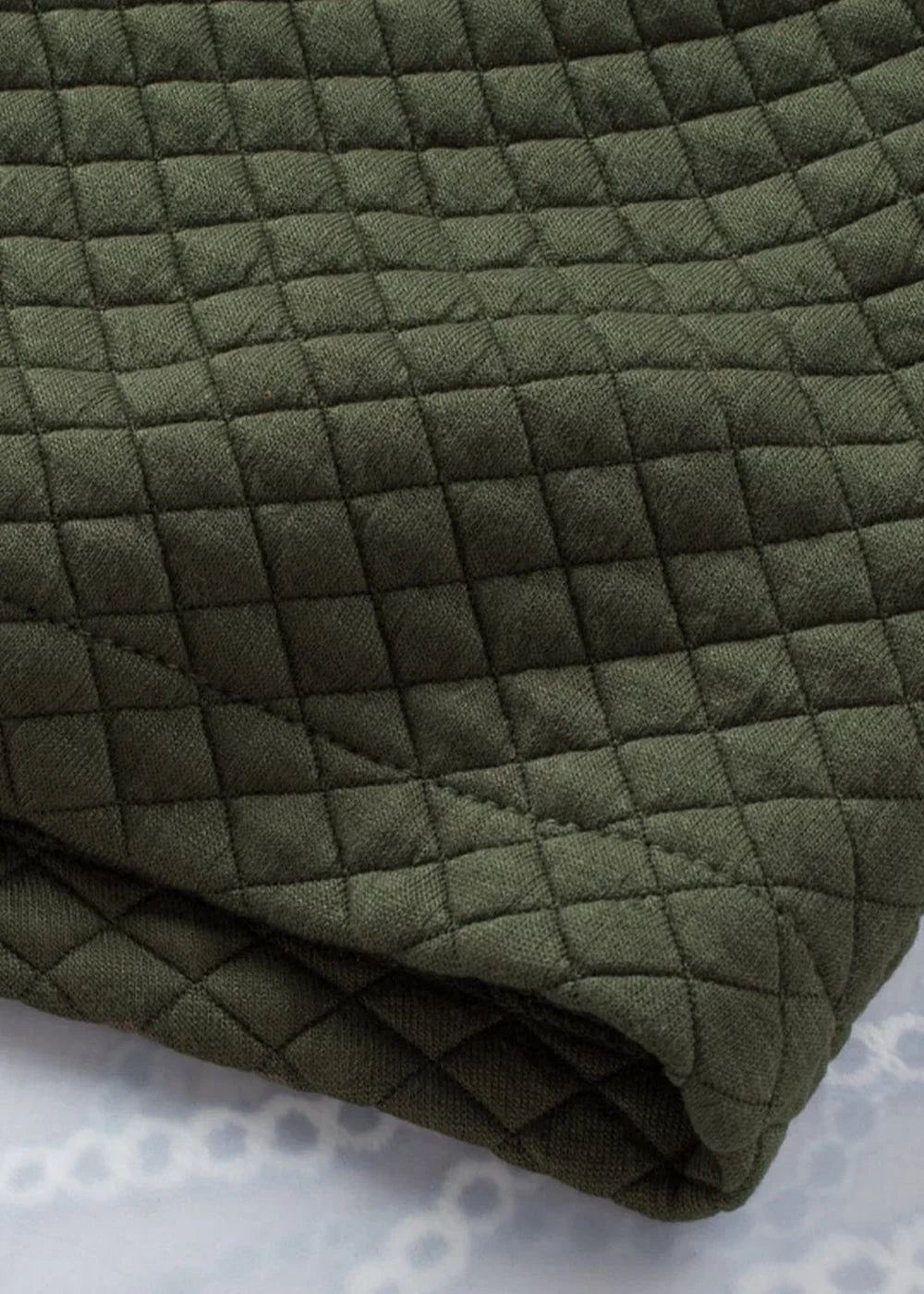 Close-up of quilted olive green fabric with a diamond pattern, showing texture and a folded edge.
