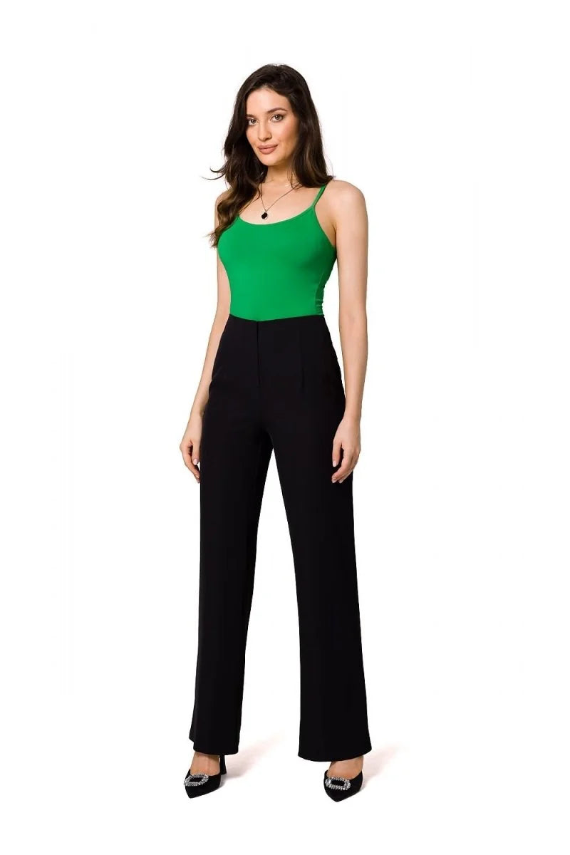 Black wide-leg trousers with a high waist and subtle pleats, worn by a model with a green top and embellished black heels.