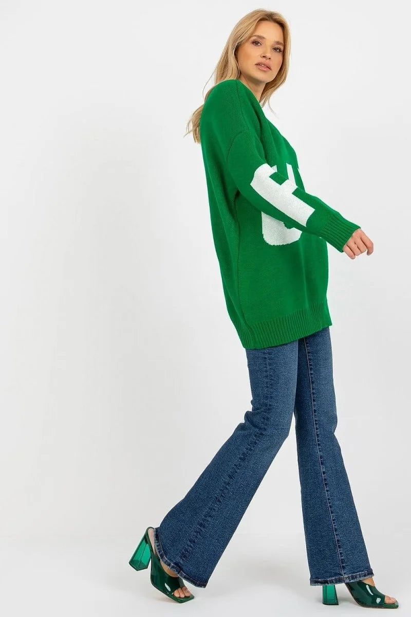 Green knit sweater with white graphic detail on sleeve, worn with dark wash flare jeans and green block heel mules.