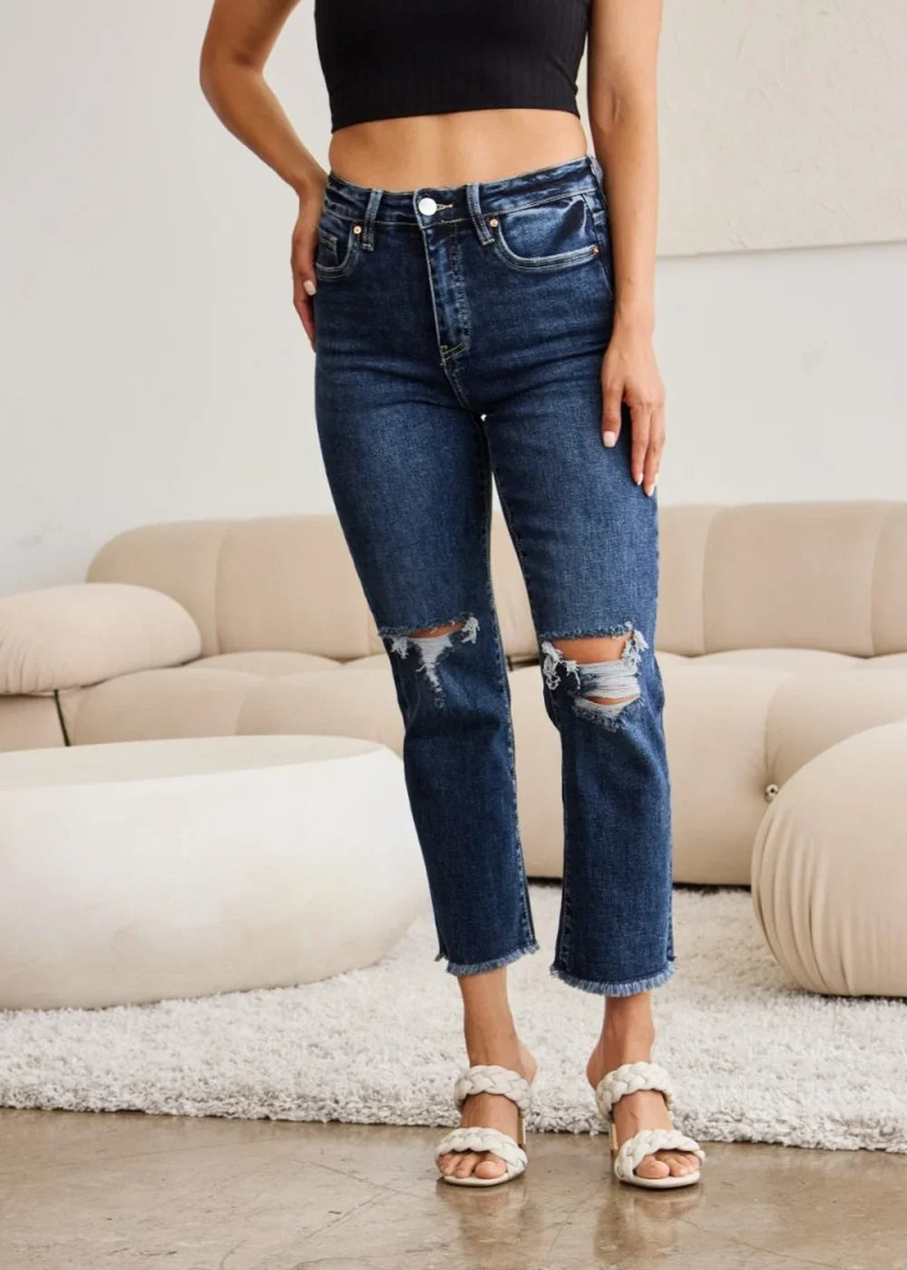 Dark wash distressed denim jeans with a frayed hem and ripped knees, on a model.