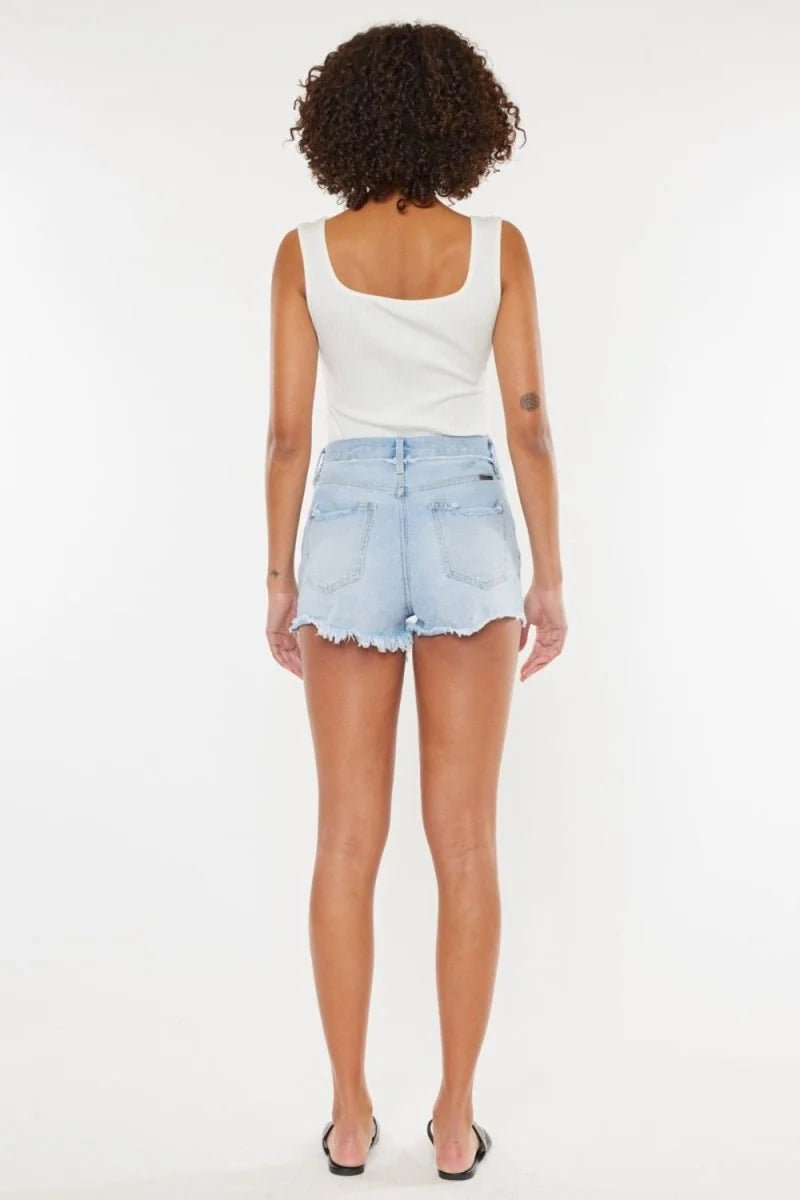 Back view of light wash denim shorts with a frayed hem and distressed details on a model.