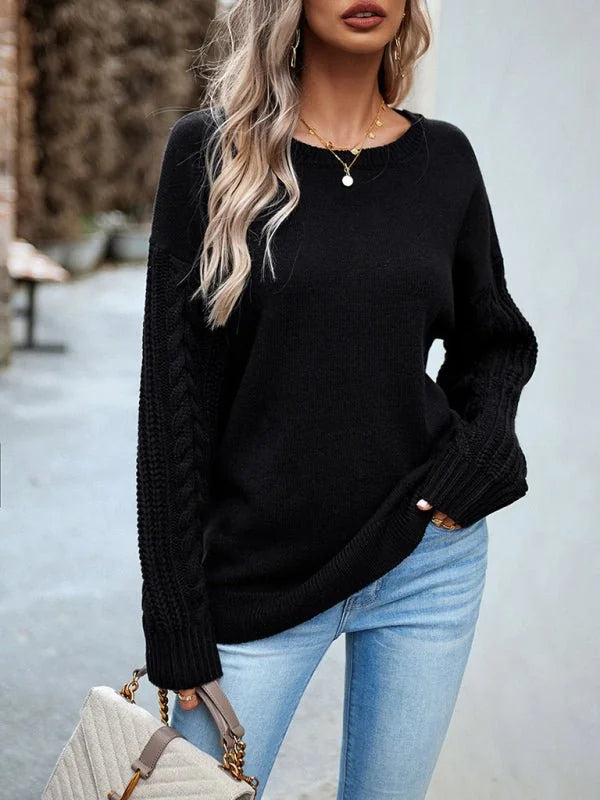 Black knit sweater with cable knit sleeves, paired with light wash jeans.