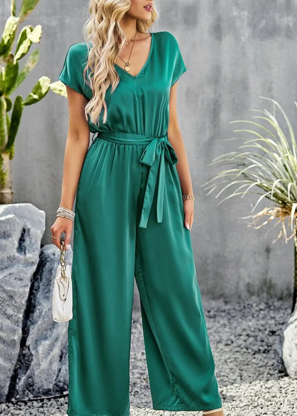 Emerald green satin jumpsuit with a V-neck, tie waist, and wide legs, worn by a model.