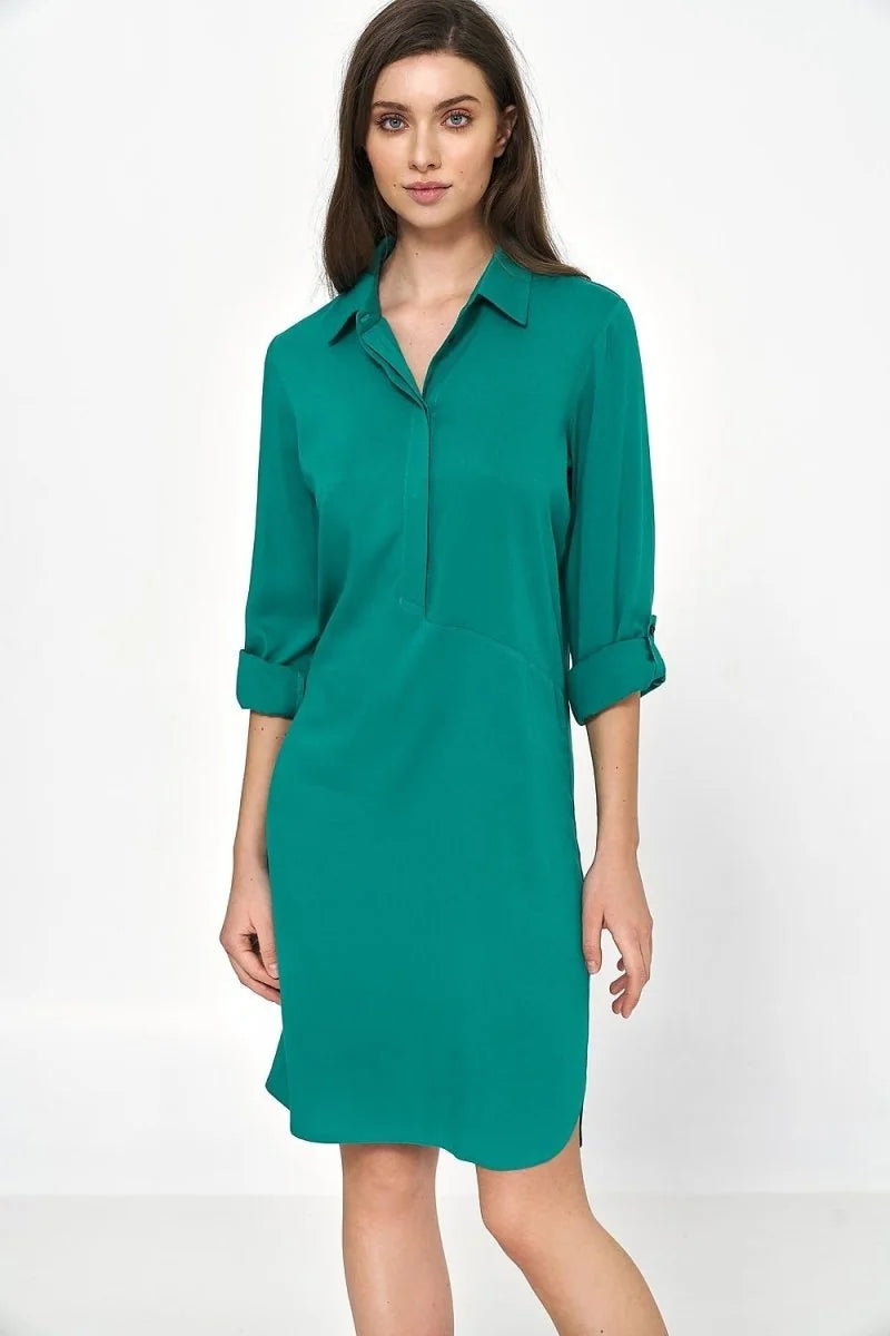 Woman in oversized emerald green viscose shirt dress with rolled-up sleeves.