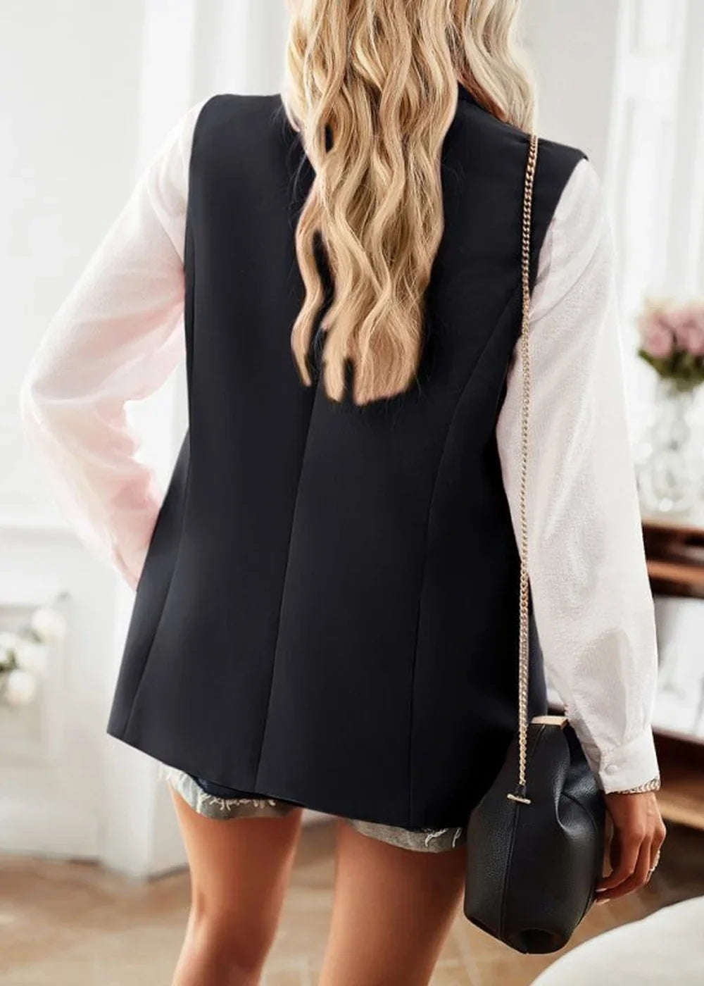 Black sleeveless blazer worn over a white long-sleeve shirt, showing the back and a black purse.