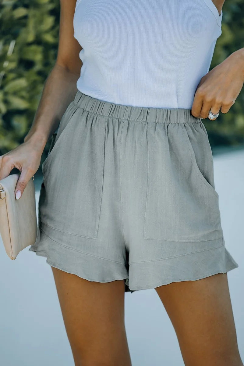 Light olive green linen-blend shorts with elastic waistband, pockets, and ruffle hem on model.